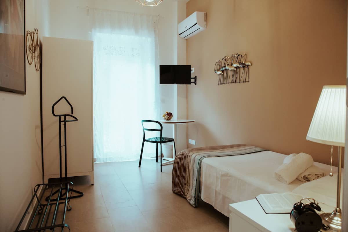 A hotel room with a bed, a desk, a chair, a TV, and a wall-mounted air conditioner.