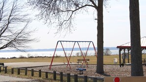 A playground with swings and a bench, surrounded by trees and a body of water in the background. - Chesapeake Bay Loft Retreat, Walk to Water, Sleeps 2,  20 Min to Annapolis (Deale)
