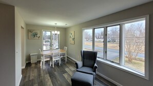 A dining area with a table and chairs, a window with a view of a parking lot and buildings, and a large window with a view of a road and trees. - Chesapeake Bay Loft Retreat, Walk to Water, Sleeps 2,  20 Min to Annapolis (Deale)