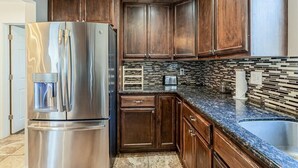 A kitchen with dark wooden cabinets, a stainless steel refrigerator, a tiled backsplash, and a granite countertop.