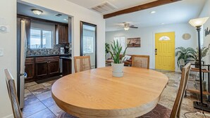 A spacious dining area with a large round table, wooden chairs, and a potted plant.