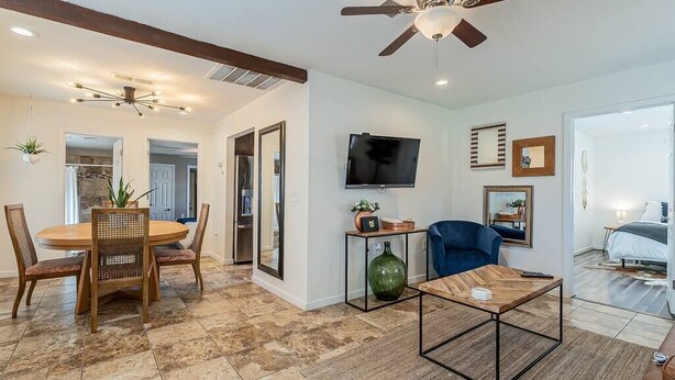 A modern living room with a dining area, a TV mounted on the wall, and a ceiling fan.