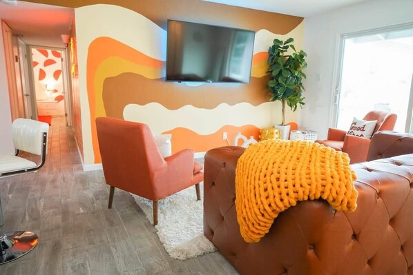 A modern living room with a large TV, comfortable seating, and a decorative wall. - Groovy Getaway - 70s themed house! (Phoenix)