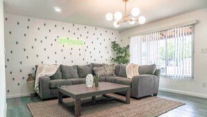 Ein Wohnzimmer mit einem grauen Ecksofa, einem Holztisch, einem Webteppich und einer Wand mit Kaktusmuster.