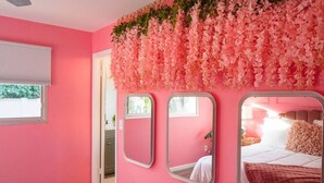 Ein rosafarbenes Zimmer mit einem Bett, einem Spiegel und einem Fenster.