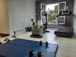 Ein Fitnessraum mit Trainingsgeräten, darunter ein Laufband, Crosstrainer und Gewichte.