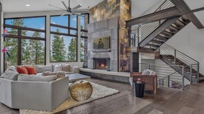 A modern living room with a fireplace, large windows, and a staircase. - Hot Tub + Ski Shuttle | Vickery's Vantage (Breckenridge)