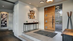 A modern reception area with a wooden door, a console table with a plant, and a geometric wall art piece.