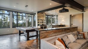 Un vaste espace de vie comprenant une table de billard, un coin salon confortable et une cuisine dotée d’une grande fenêtre.