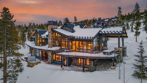 Un grand chalet à plusieurs étages, doté d’une vaste terrasse et d’un bain à remous, entouré de neige et d’arbres.