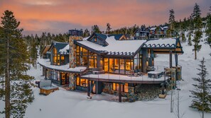 Un grand chalet à plusieurs étages, doté d’une vaste terrasse et d’un bain à remous, entouré de neige et d’arbres.