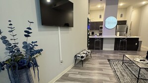 Una sala de estar moderna con un televisor de pantalla plana en la pared, una planta grande en maceta y una zona de bar con taburetes.