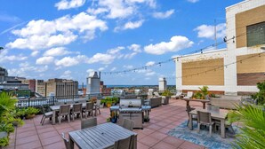 Una terraza en la azotea con mobiliario exterior, una parrilla y luces colgantes.