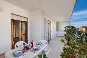 Un coin repas avec une table dressée pour quatre personnes, des chaises blanches et une vue sur le paysage urbain à travers une porte vitrée.