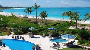 Zona de piscina con sillones de descanso y sombrillas, con vista a una playa y al océano.