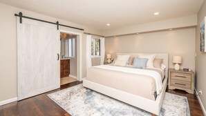 Une chambre à coucher avec un grand lit, une table de chevet, une commode et une porte coulissante donnant sur une autre pièce.