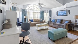 A modern living room with a ceiling fan, two sofas, a coffee table, and a desk with a lamp. - Pool, Spa, Playground and More at Villas at Laguna Bay!! (Kissimmee)