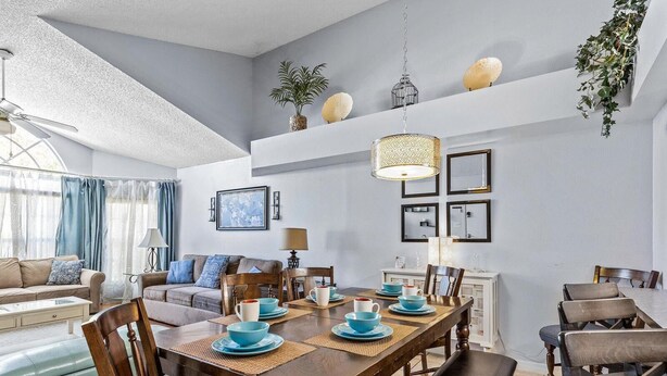 A dining area with a wooden table set for four, surrounded by chairs. There is a sofa and a lamp in the background. - Pool, Spa, Playground and More at Villas at Laguna Bay!! (Kissimmee)
