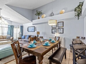 A dining area with a wooden table set for four, surrounded by chairs. There is a sofa and a lamp in the background. - Pool, Spa, Playground and More at Villas at Laguna Bay!! (Kissimmee)