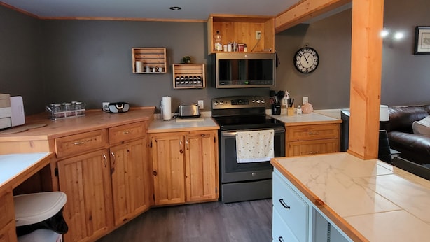 A compact kitchen with wooden cabinets, a built-in oven, a microwave, and a clock on the wall. - Naini's Rental, 4 bedrooms, located on Deer Island, N.B. 5 mins from the water. (Lords Cove)