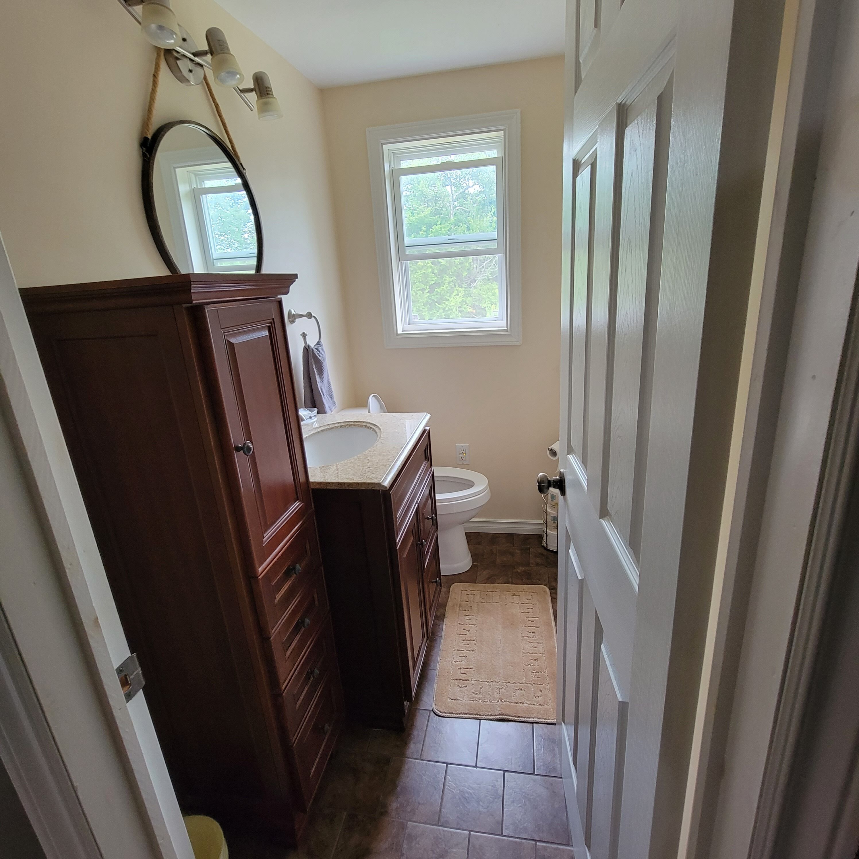 A bathroom with a wooden vanity, a toilet, a window, and a door.