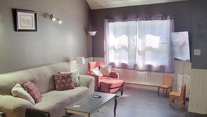 A modern living room with a sofa, a dining table, and a TV. - Naini's Rental, 4 bedrooms, located on Deer Island, N.B. 5 mins from the water. (Lords Cove)