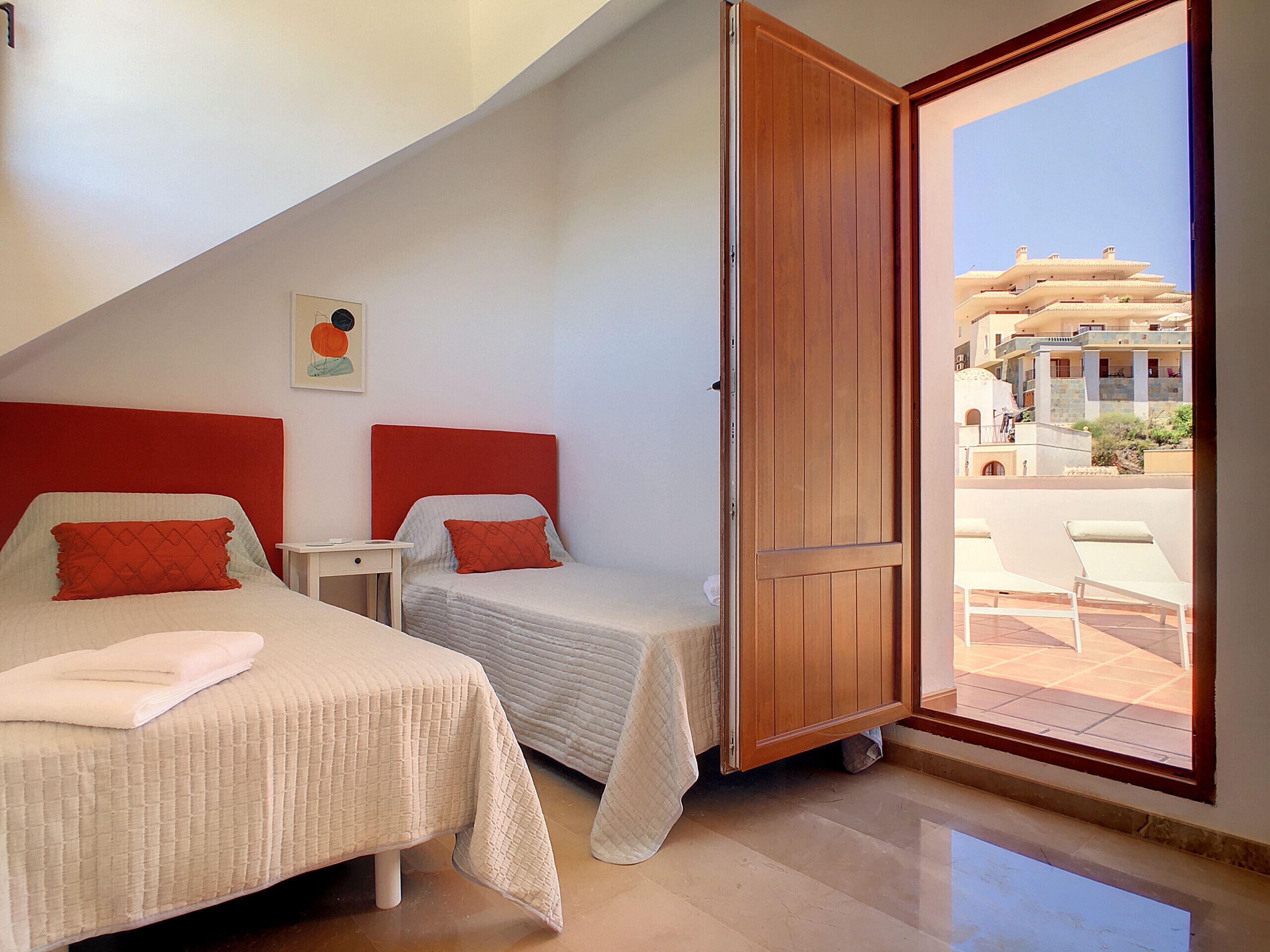 A hotel room with two beds, a wooden door, and a view of the outside.