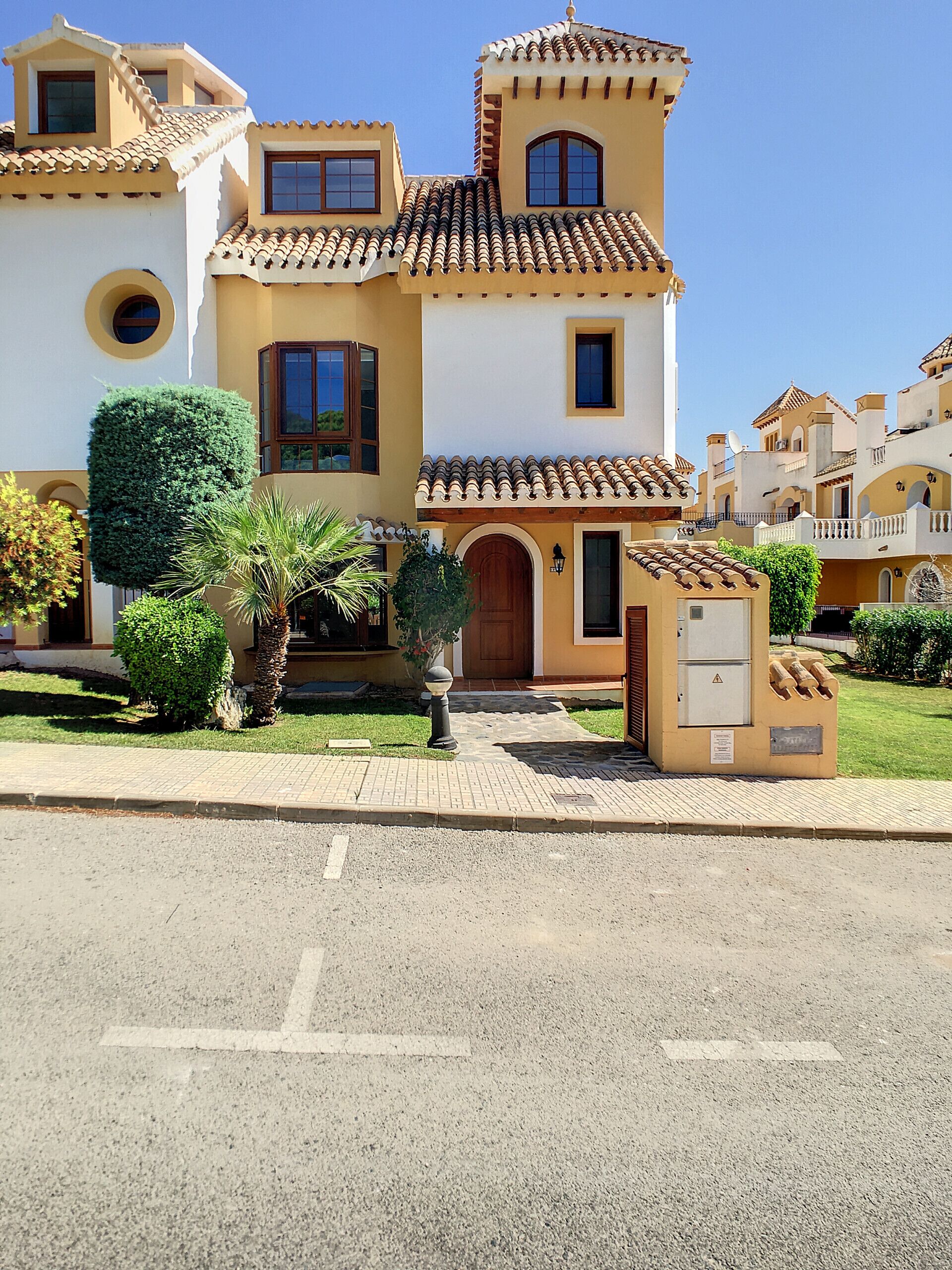 A two-story house with a tiled roof, a small balcony, and a well-maintained lawn.