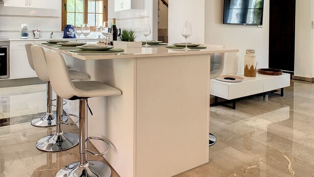 Een moderne keuken met een centraal eiland, barkrukken, hanglampen en een flatscreen televisie aan de muur.