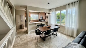A modern kitchen with a dining area, a staircase, and a large window with curtains. - Beautiful Beach Longboat Key Townhouse (Longboat Key)