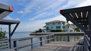 A wooden dock leading to a building with a light blue facade, a pool, and a clear view of the sea. - Beautiful Beach Longboat Key Townhouse (Longboat Key)