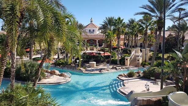 A resort with a central pool, palm trees, and a building with a red roof. - 3 bedroom villa (Sleeps 8) in a tropical Tuscan style resort near Disney (Davenport)