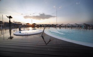 En swimmingpool med ett trädäck, ett bubbelbad och parasoller i bakgrunden.