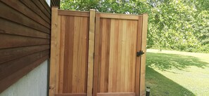 A wooden gate with a black handle, set against a backdrop of a green lawn and trees.