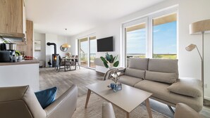 A modern living room with a sofa, coffee table, and a dining area with a TV. - "BeachLoungeThree" vacation apartment on the beach with sun terrace, sauna & sea view (Olpenitz)