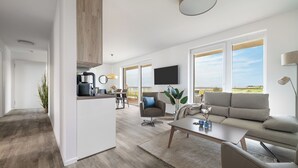 A modern living space with a kitchen, dining area, and a large window offering a view. - "BeachLoungeThree" vacation apartment on the beach with sun terrace, sauna & sea view (Olpenitz)