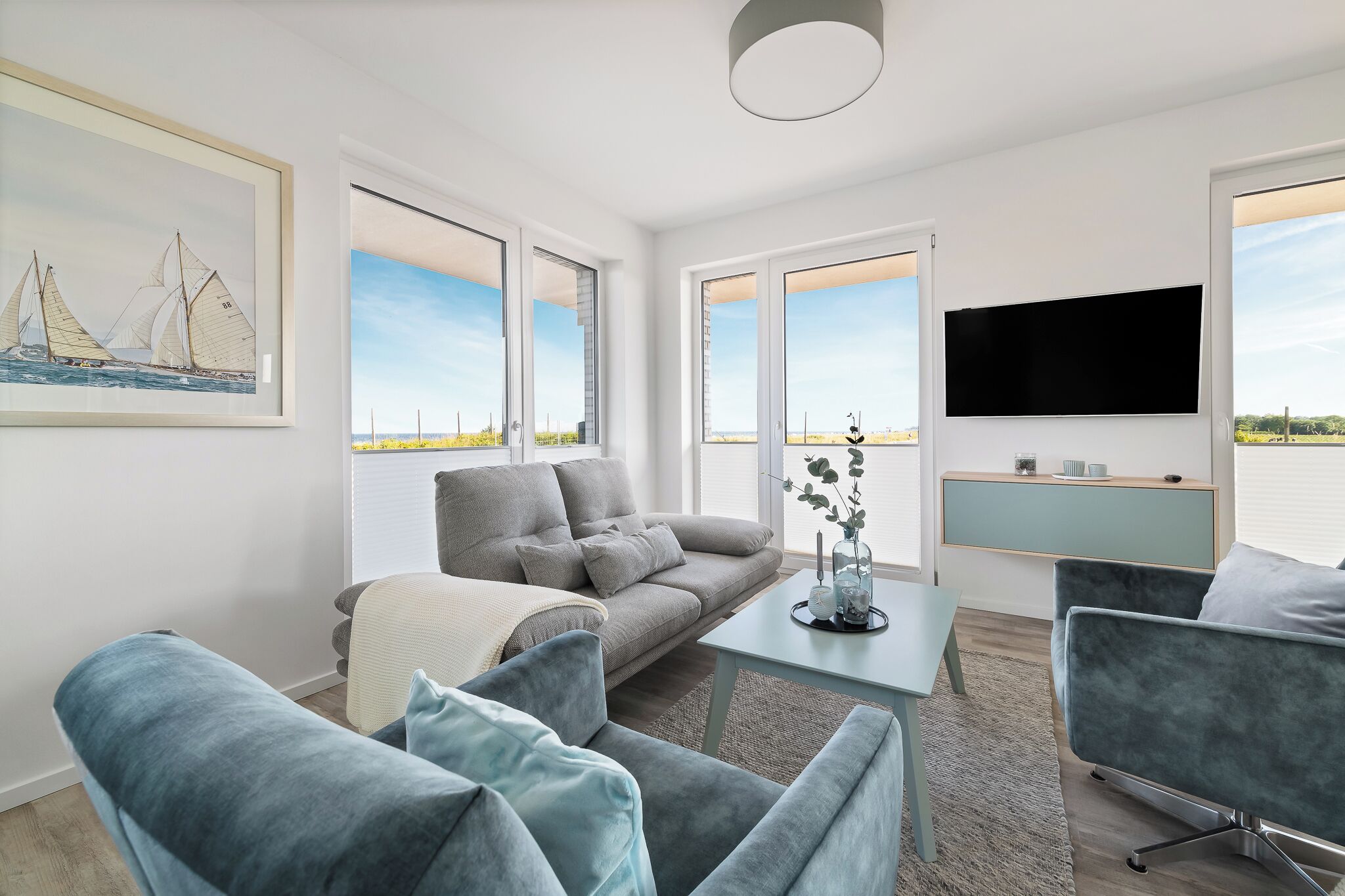 A modern living room with a grey sofa, blue armchairs, a coffee table, and a flat-screen TV mounted on the wall.