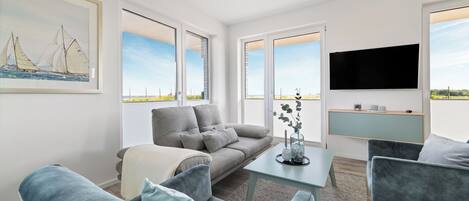 A modern living room with a grey sofa, blue armchairs, a coffee table, and a flat-screen TV mounted on the wall.