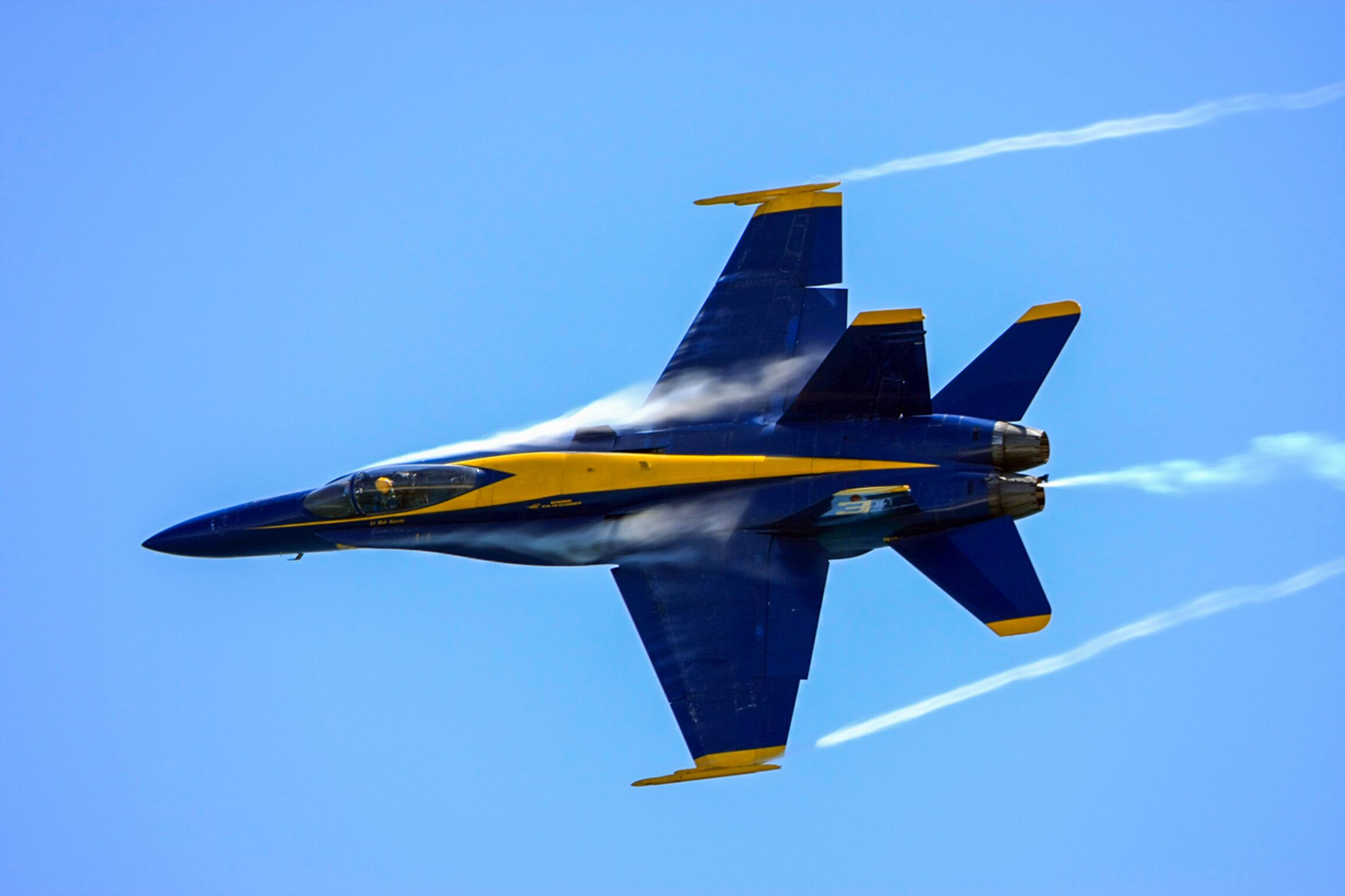 Un avión jet azul y amarillo en vuelo, dejando estelas contra un cielo azul despejado.