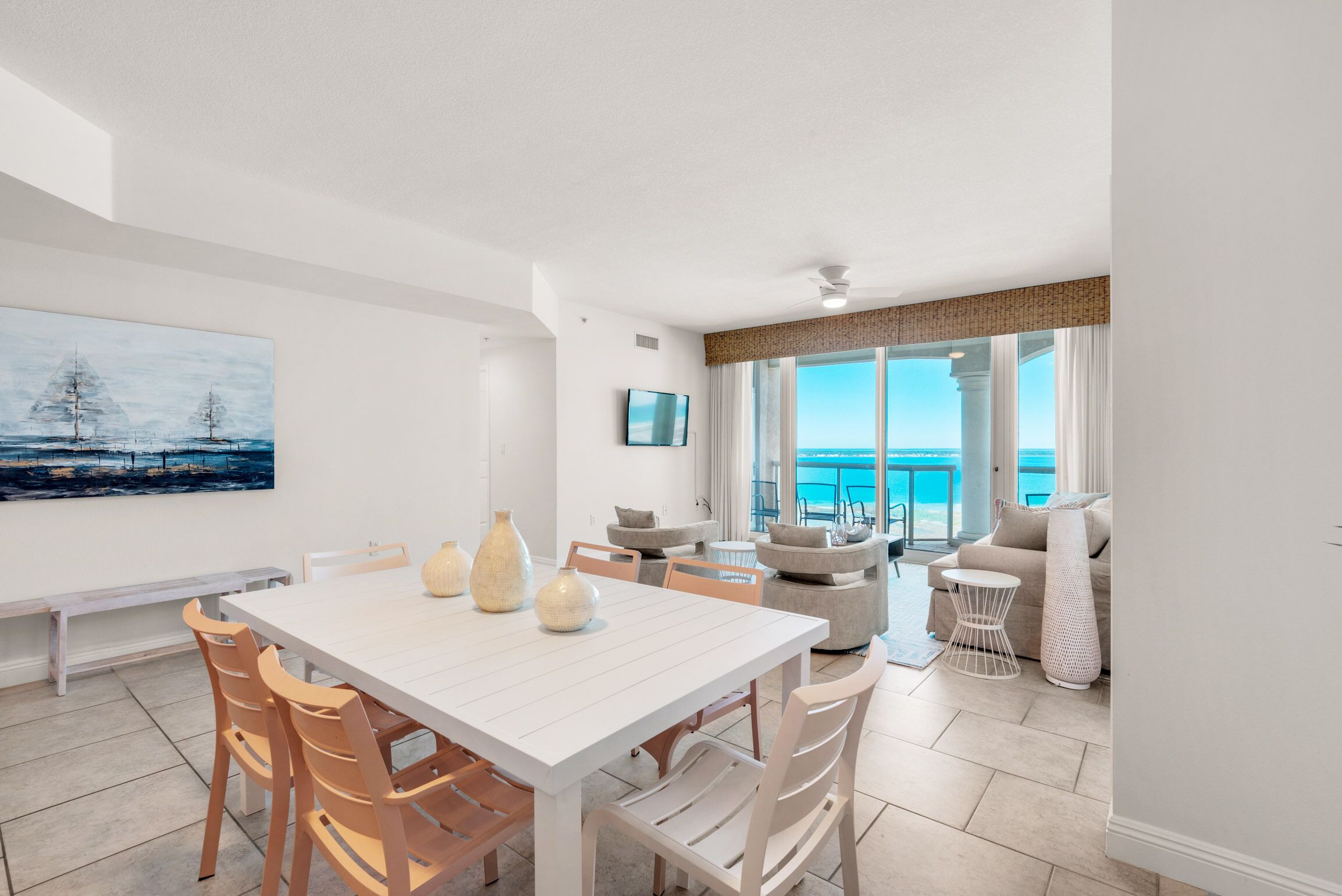 Un moderno salón con una mesa de comedor blanca, sillas de madera y un gran ventanal con vistas al mar.