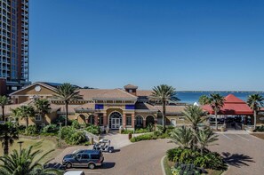 A hotel with a central entrance, palm trees, and a view of the sea.