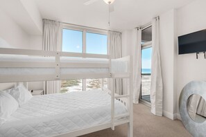 A bunk bed room with a TV, a circular mirror, and a view of the beach.