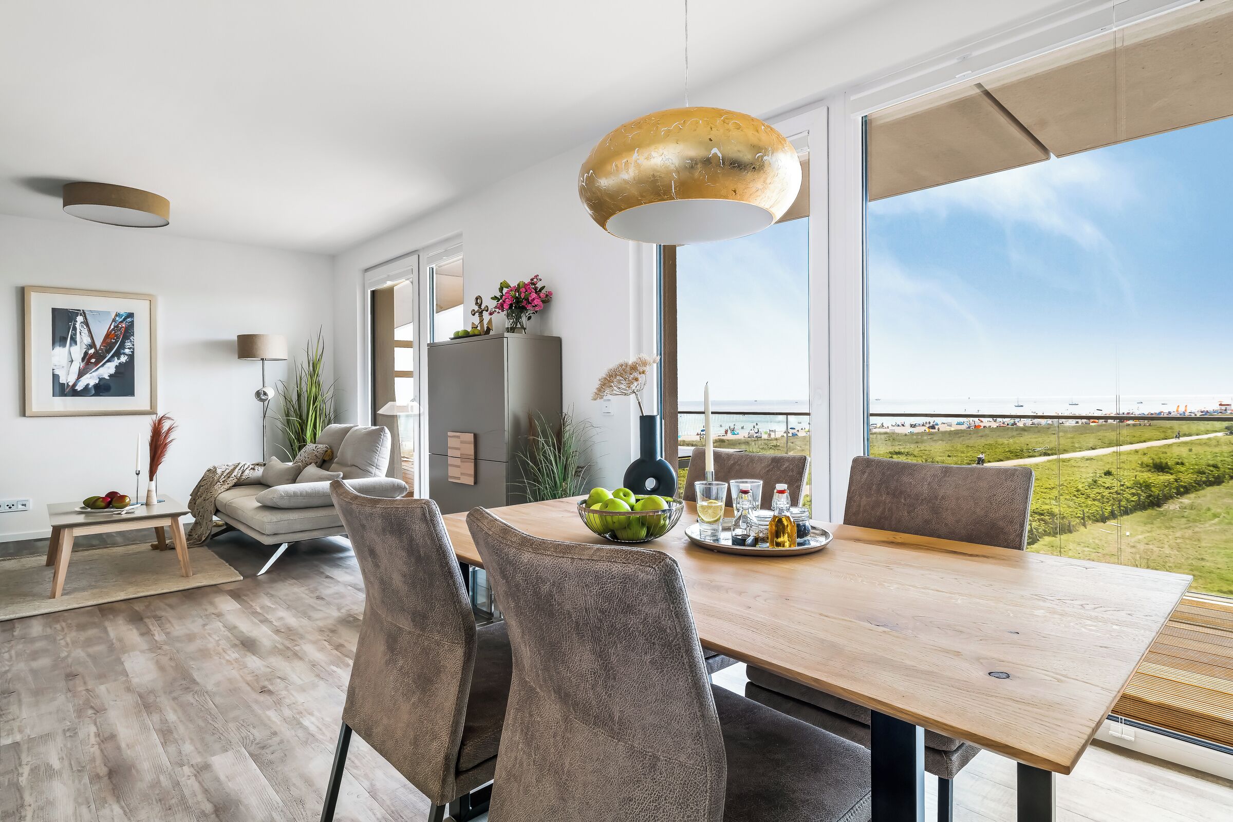 A modern dining area with a wooden table, grey upholstered chairs, and a large window offering a view of the landscape.