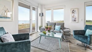 Een ruime woonkamer met een groot raam, een bank, een salontafel en uitzicht op het strand.