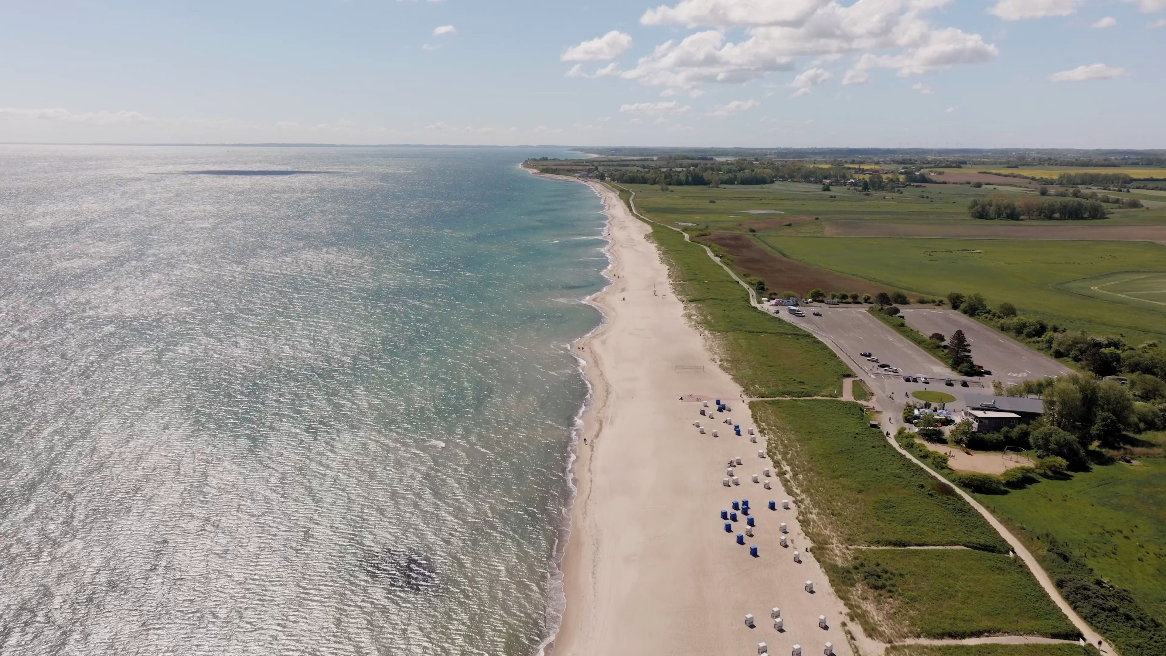 An aerial view of a beach with a parking lot and buildings.