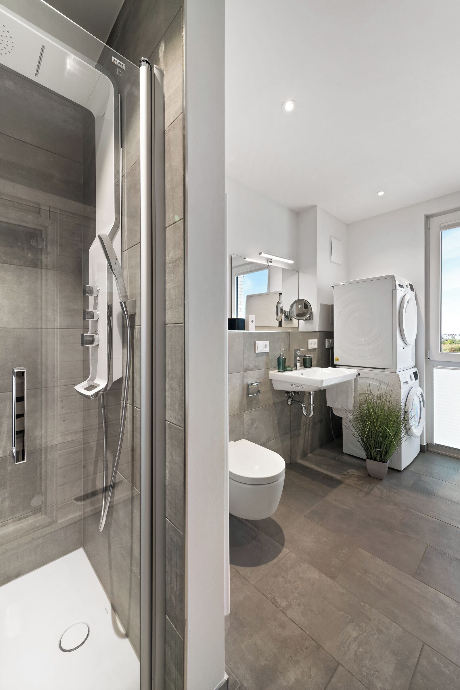 Ein modernes Badezimmer mit einer Duschkabine, Toilette, Waschbecken sowie gestapelten Waschmaschine und Trockner.
