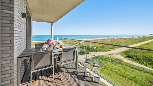 Een balkon met een tafel en stoelen, met uitzicht op een strand en de oceaan.