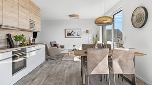 A modern kitchen with white cabinets, a built-in oven, and a dining area with a wooden table and chairs. - "BeachViewTwo": Holiday apartment right on the beach with sauna, balcony & Baltic Sea view (Olpenitz)