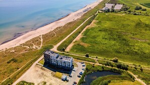 An aerial view of a coastal property with a beach, a parking area, and a building with multiple floors. - "BeachViewTwo": Holiday apartment right on the beach with sauna, balcony & Baltic Sea view (Olpenitz)