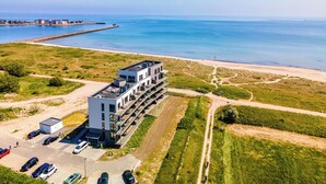 An aerial view of a modern hotel with a rooftop pool, adjacent to a beach and ocean. - "BeachViewFour": Holiday apartment right on the beach with sauna, balcony & Baltic Sea view (Olpenitz)